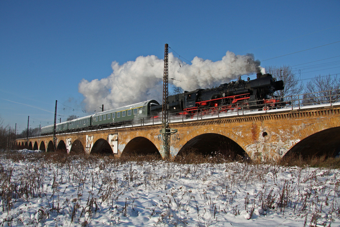 Das Bild zeigt den Museumszug mit Dampflok des Eisenbahnmuseums Leipzig auf einer Steinbrücke bei voller Fahrt.