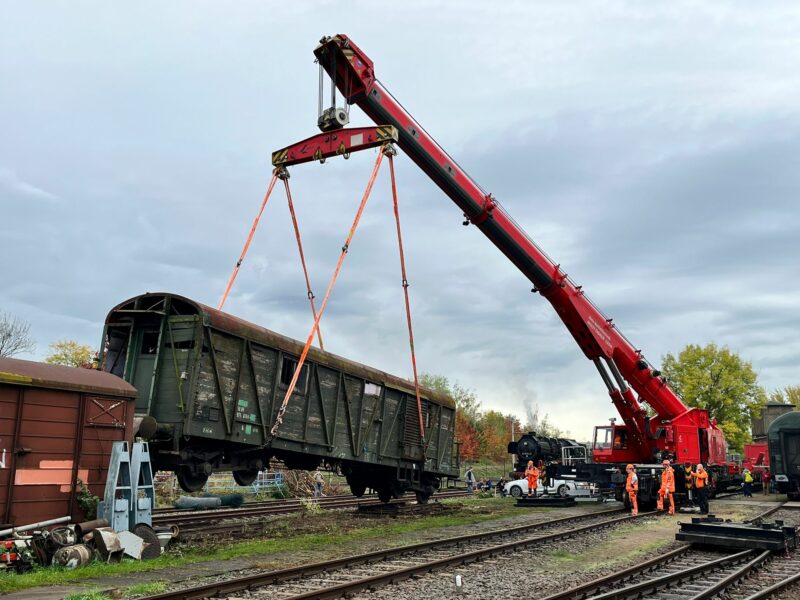 Sie sollten sehen: Multitasker 1200 der Firma Kirov aus Leipzig hebt Werkstattwagen ins Gleis. Der Wagen schwebt gearde über dem Gleis und wird langsam abgesetzt.