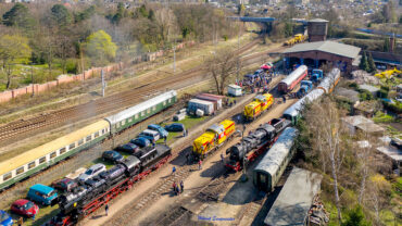 Sie sollten sehen: das Gelände des Eisenbahnmuseums Leipzig aus der Luft. Es herrscht reges Treiben. Neben zwei Dampflokomotiven der Baureihe 52.8 sind zwei V100 der MEG (Mitteldeutsche Eisenbahngesellschaft) zu sehen. Am südlichen Ende (oberer Bildrand) ist der Lokschuppen mit vier Gleisen zu sehen. Die benannten Fahrzeug sehen auf den Gleisen.