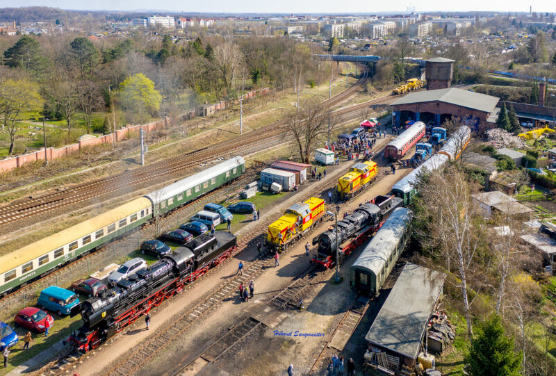 Sie sollten sehen: das Gelände des Eisenbahnmuseums Leipzig aus der Luft. Es herrscht reges Treiben. Neben zwei Dampflokomotiven der Baureihe 52.8 sind zwei V100 der MEG (Mitteldeutsche Eisenbahngesellschaft) zu sehen. Am südlichen Ende (oberer Bildrand) ist der Lokschuppen mit vier Gleisen zu sehen. Die benannten Fahrzeug sehen auf den Gleisen.