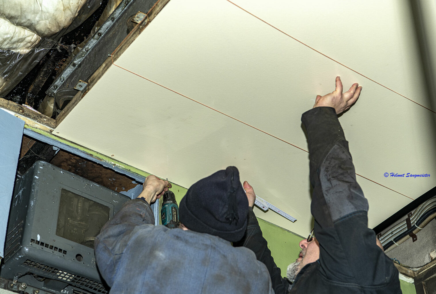 Sie sollten sehen: wie zwei Mitarbeiter des Eisenbahnmuseums ein großen Deckenpanel montieren. Einer schraubt, der andere hält das Panel mit ausgestreckten Armen an der Decke. Die Lage der Leisten zur Befestigung ist durch gespannte Fäden markiert.