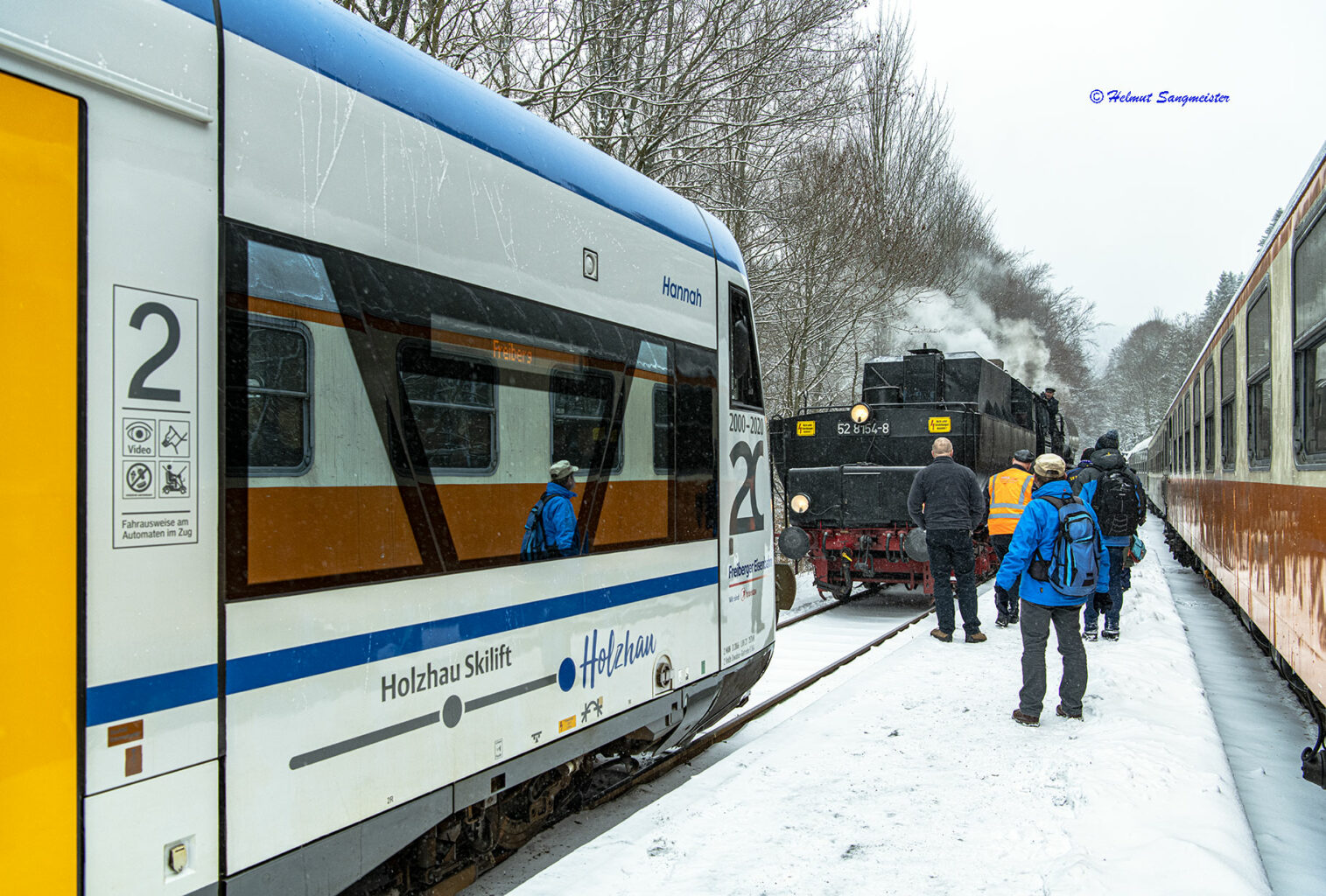 Sie sollten sehen: die Situation im Bahnhof Holzhau vom mittleren Bahnsteig aus. Links steht ein moderener Triebwagen, weiter im Hintergrund die Dampflok 52 8154 mit Blick auf den Tender. Rechts flankiert ein Städtexpress-Wagen der Gattung Ame das Bild. Besonderheit der Städtexpresswagen ist die Farbgebung in Orange unten und Elfenbein auf Fensterhöhe. 