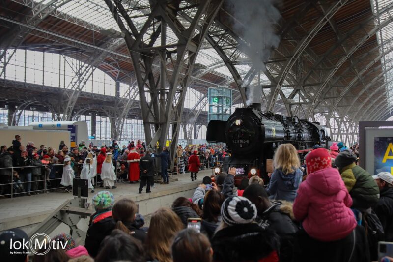 Das Bild zeigt eine Menschenmenge auf dem Leipziger Hauptbahnhof, welche den Weihnachtsmann willkommen heißen. Zahlreiche Kinder und Eltern sehen gebannt auf die Einfahrt der Dampflokomotive des Leipziger Eisenbahnmuseums.
