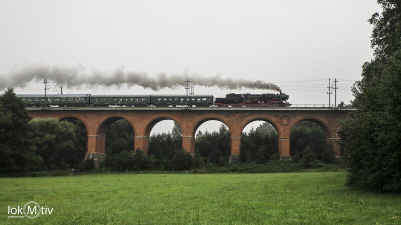 Das Bild zeigt die Seitenansicht des in Backstein erbauten Viaduktes in Steinpleis. Die Dampffahne von 52 8154 zieht über den Leipziger Museumszug.