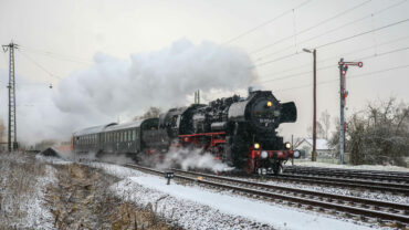 Das Bild zeigt einen Dampfzug in voller Fahrt bei leichtem Schnee. Rechts im Bild ein Formsignal.