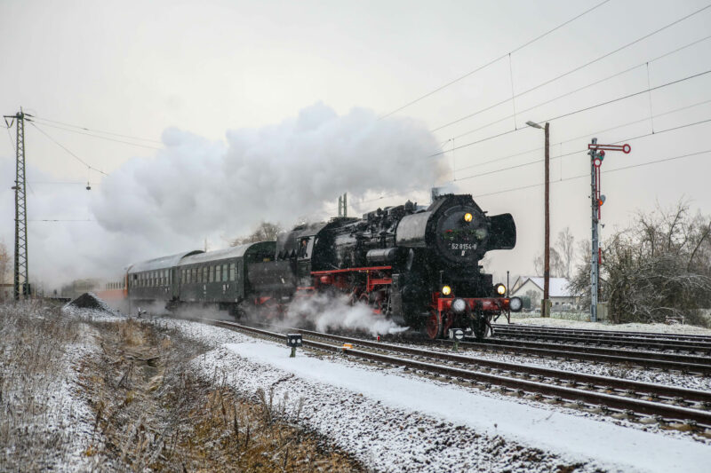 Das Bild zeigt einen Dampfzug in voller Fahrt bei leichtem Schnee. Rechts im Bild ein Formsignal.