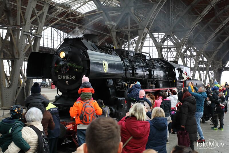 Das Bild zeigt eine Menschenmenge auf dem Leipziger Hauptbahnhof, welche den Weihnachtsmann willkommen heißen. Zahlreiche Kinder und Eltern sehen gebannt auf die Einfahrt der Dampflokomotive des Leipziger Eisenbahnmuseums.