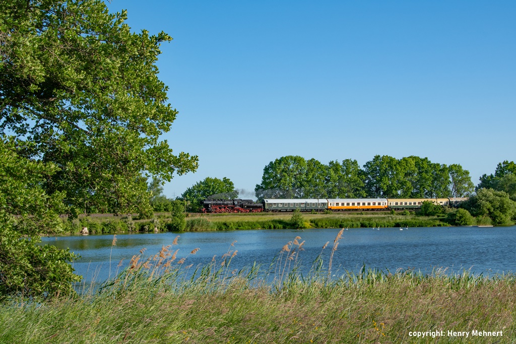 Das Bild zeigt den Museumszug des Eisenbahnmuseums Leipzig in der wunderschönen sommerlichen Landschaft. Im Vordergrund ein See mit Schwänen.
