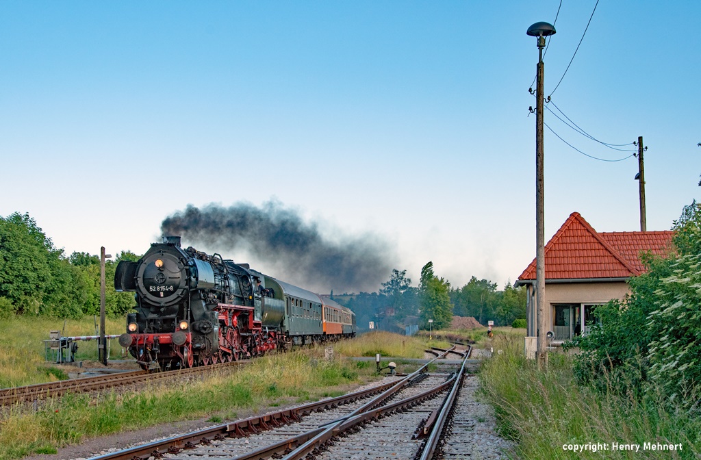 Das Bild zeiggt den Museumszug des Eisenbahnmuseums Leipzig mit der Dampflokomotive 52 8154 bei der Durchfahrt in Caaschwitz. Rechts im Bild das Stellwerk und eine Pilzlampe.