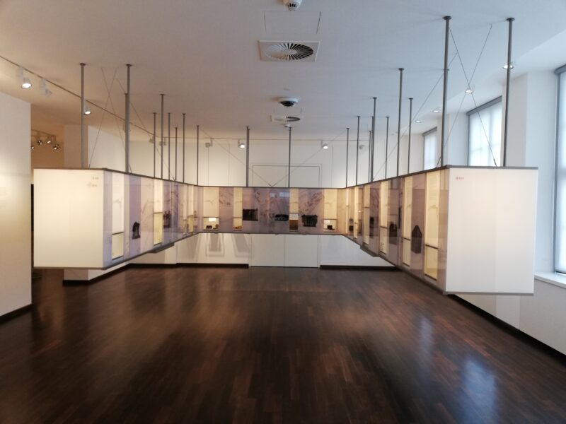 Das Bild zeigt einen Ausstellungsraum im Uhrenmuseum in Glashütte. Die Vitrinen sind hoch modern gestalltet und von der Decke abgehangen.