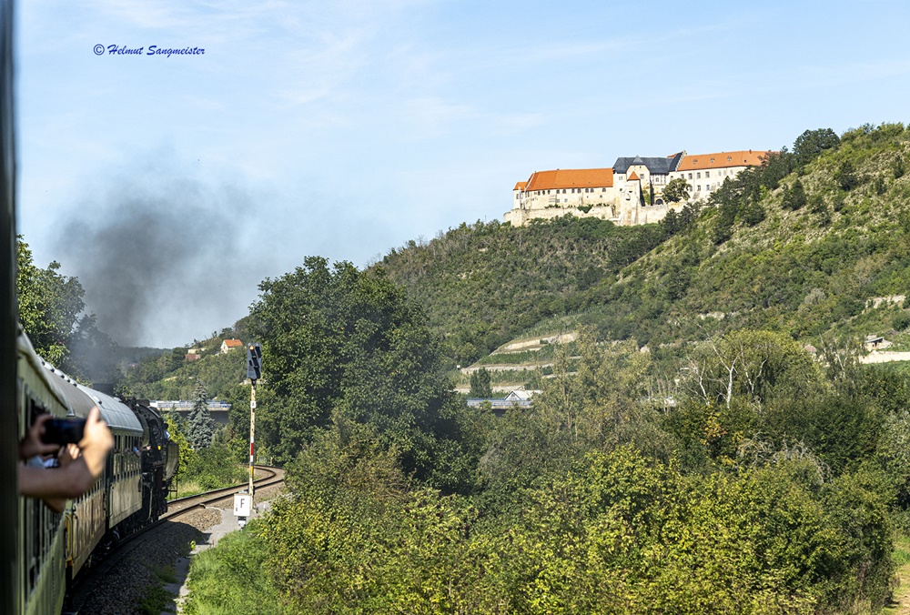 Das Bild ist aus dem fahrenden Zug aufgenommen und zeigt den sich schlängelnden Schienenweg. Rechts oberhalb auf einem Berg ist Schloß Neuenburg zu sehen.