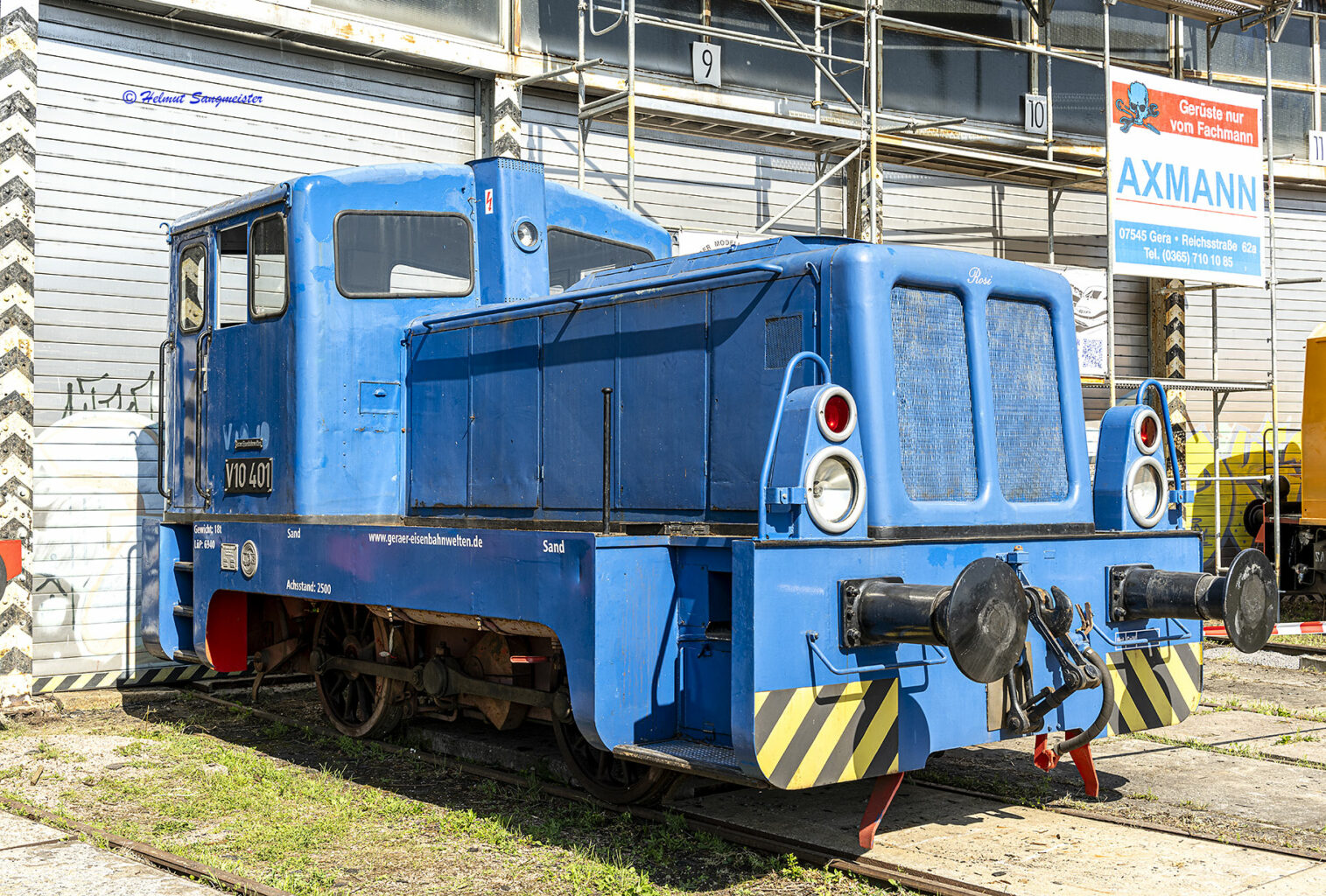 Das Bild zeigt eine Kleindiesellok der Baureihe V10 mit der Nummer 401 vor einem geschlossenen Rolltor des Rundhauses in Gera in Kavalierperspektive.