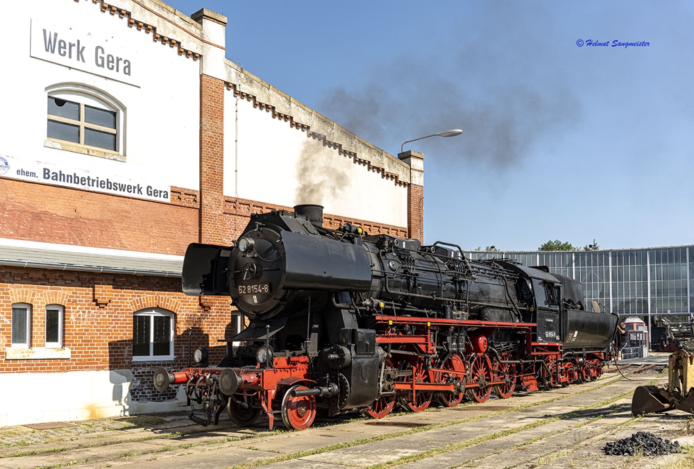 Das Bild zeigt die Dampflokomotive 52 8154 des EMBB vor der Giebelwand des Rundhauses in Gera. Am Giebel steht noch Werk Gera, ehemaliges Bahnbetriebswerk Gera.