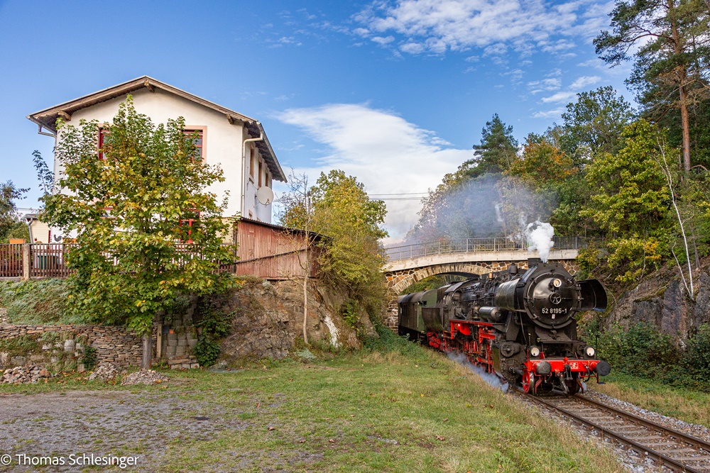 Die Dampflok 52 8195 unterquert eine aus Naturstein gebaute Bogenbrücke auf eingleisiger Strecke. Links ein Wohnhaus in überhöhter Position.