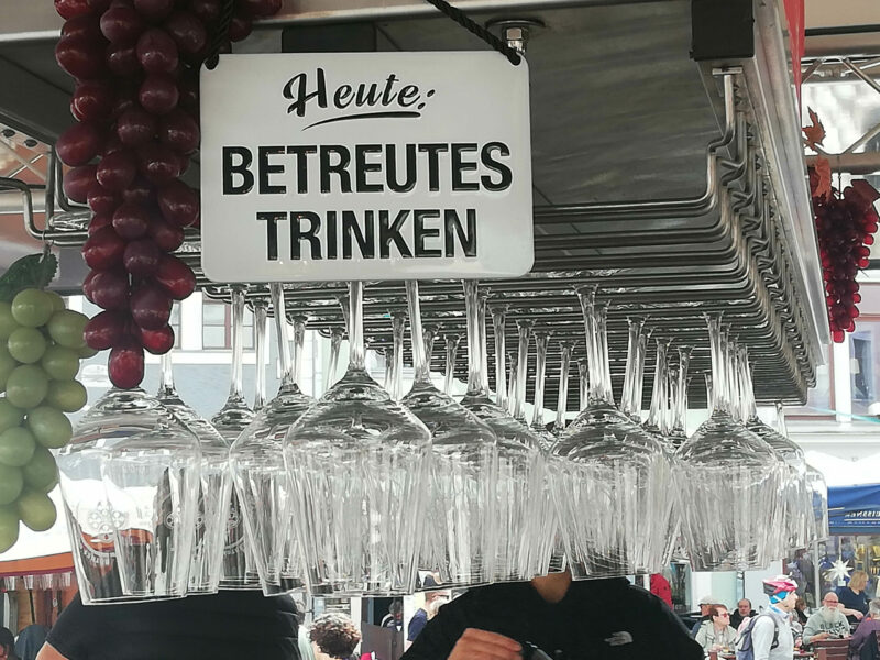 Bild zeigt ein Schild "Betreutes Trinken" und eine Menge leere Weingläser.