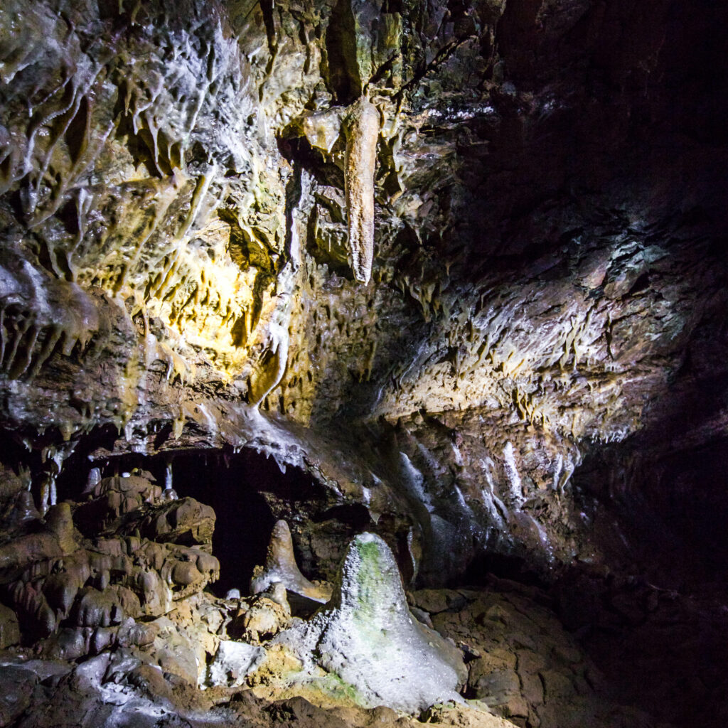 Das Bild zeigt eine Vielzahl von Stalagmiten und einen Stalaktiten in Form einer Axt. Der untere Stalagmit ist ausgetrocknet und glänzt kristallin.