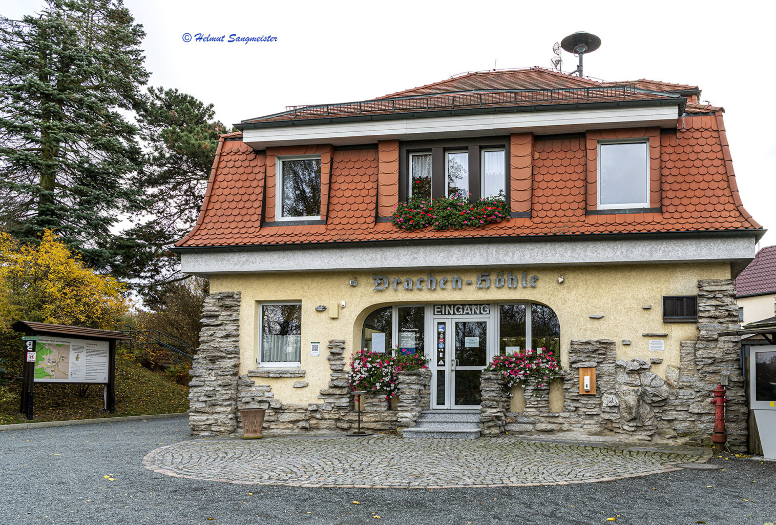 Das Bild zeigt das Empfangsgebäude der Drachenhöhle, welches eher wie ein Zwei-Familien-Haus anmutet. Die Fassade ist teilweise mit Natursteinen verkleidet.