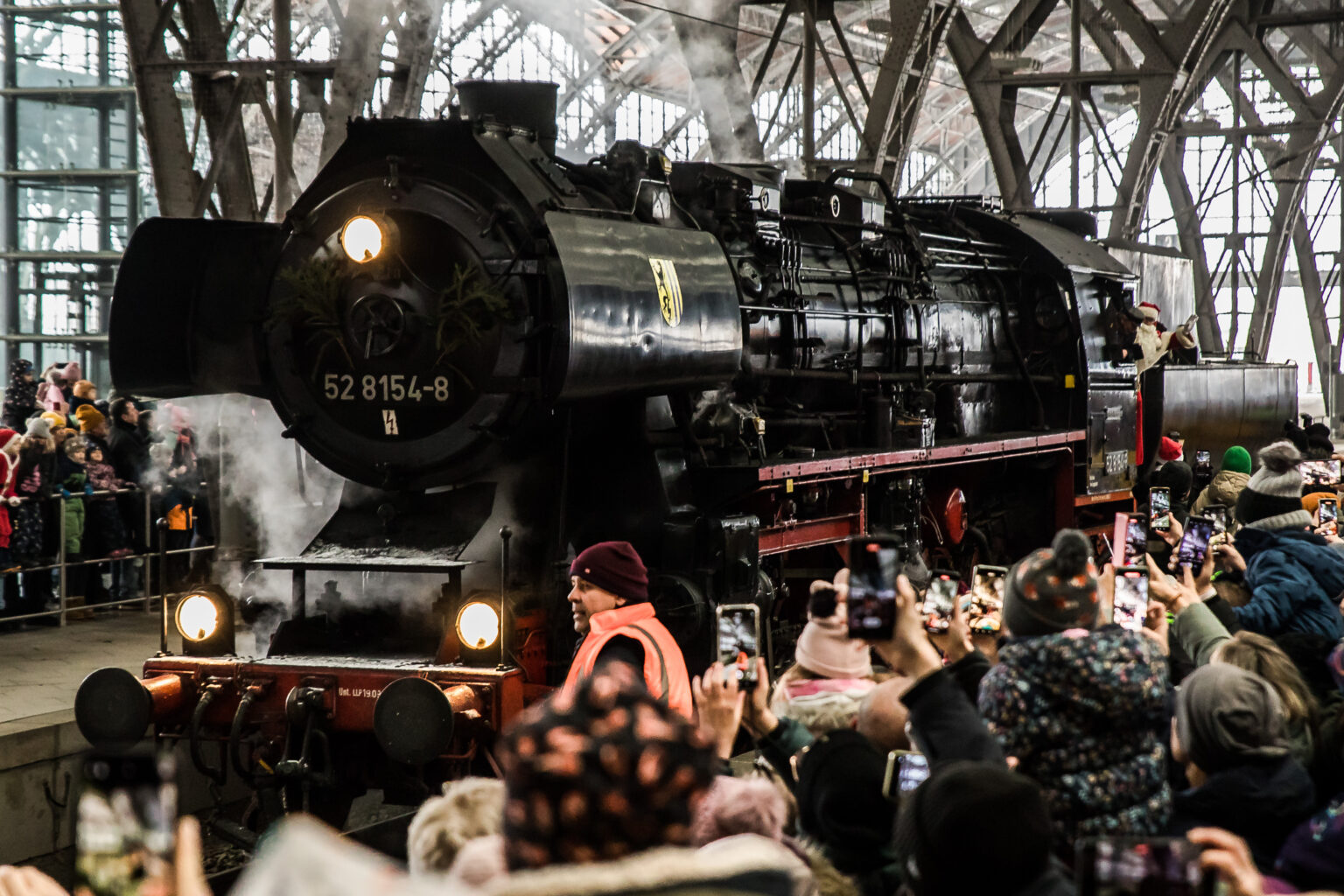 Das Bild zeigt 52 8154 in einer Menschenmenge im Hauptbahnhof Leipzig. Der Weihnachtsmann grüßt von der Lok herunter.