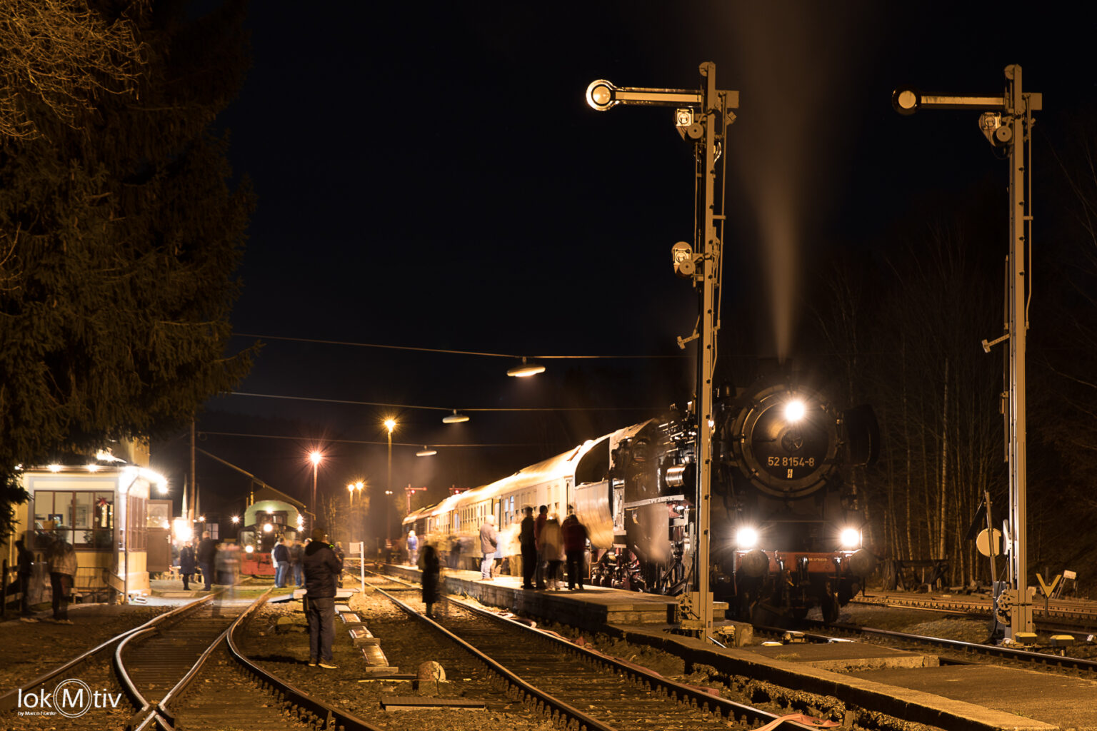 Das Bild zeigt den Museumszug bei Nacht im Bahnhof Schlettau. Vorn zwei Formsignale, links das Bahnhofsgebäude...