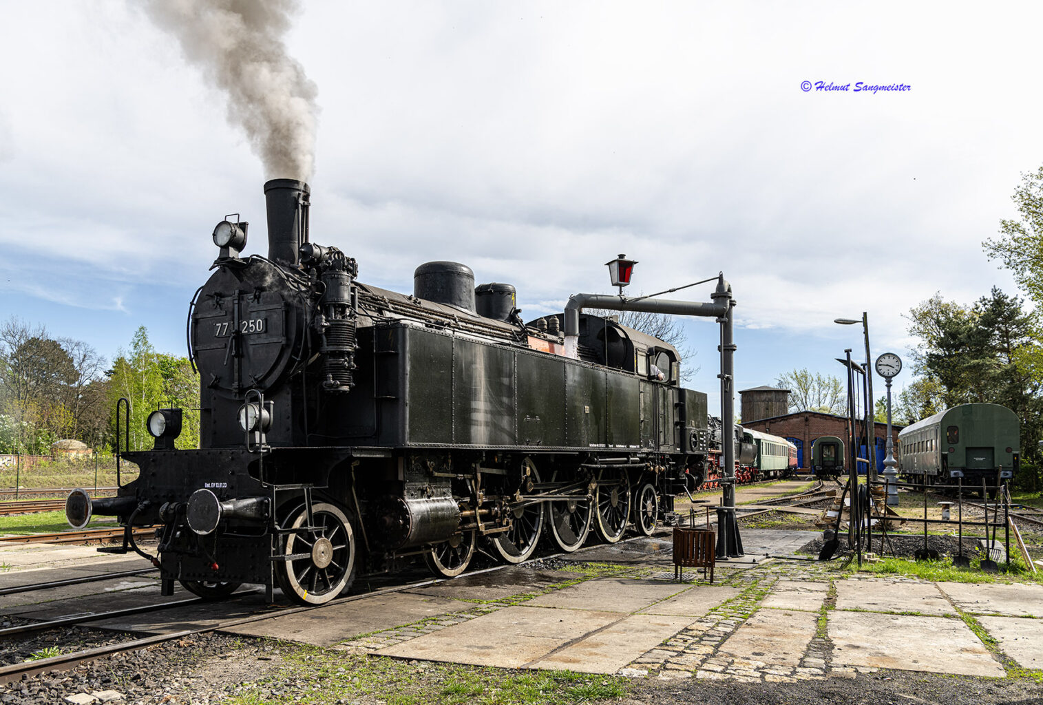 Tenderlokomotive 77.250 in völlig schwarzem Anstrich metallisch glänzenden Radreifen bekommt Wasser. Im Hintergrund der Lokschuppen.