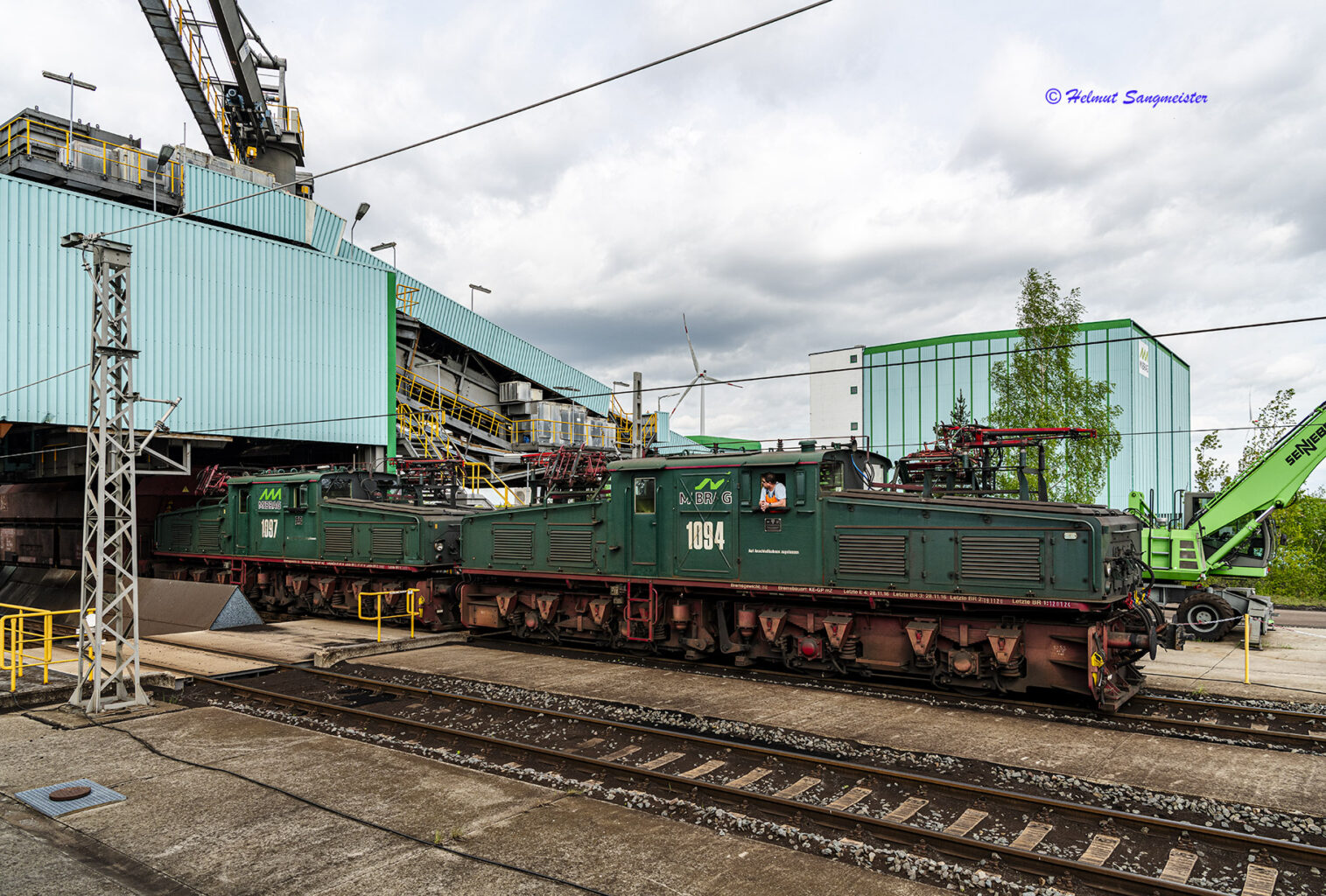 Zwei EL-2, elektrische Bergbaulokomotiven, mit einem Ganzzug aus Selbstentladewagen unter der eingehausten Förderbrücke zur Beladung mit Kohle.